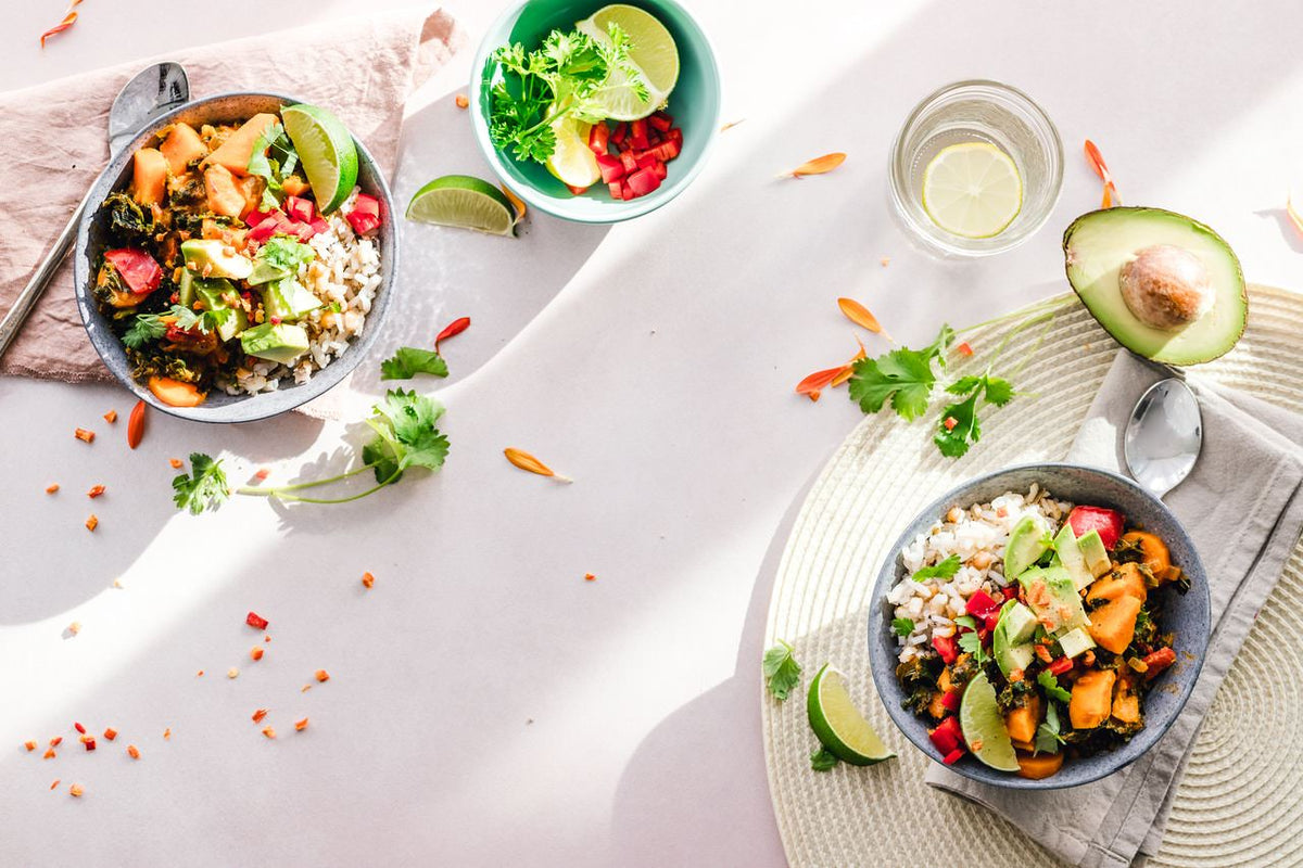 Bowls of vegetables and other foods beside avocado and a glass of water.