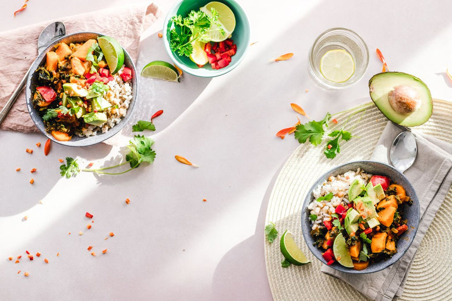 Bowls of vegetables and other foods beside avocado and a glass of water.