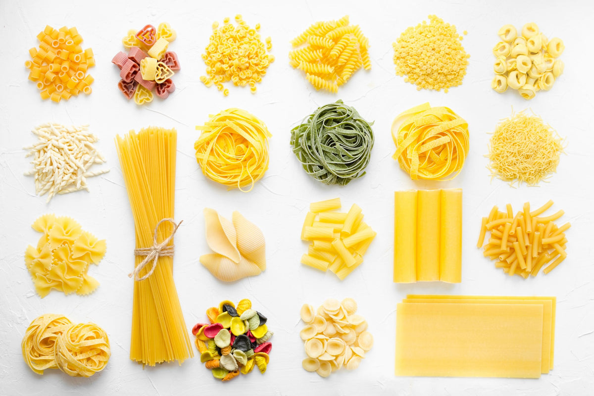 Different shapes of dry pasta arranged in rows on a white background.