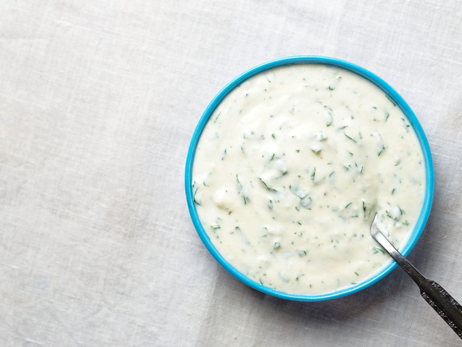 A bowl of creamy herb dressing with a spoon.