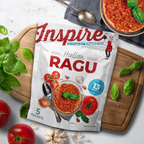 A package of Inspire Protein Kitchen Italian Ragu sits on a wooden cutting board, surrounded by fresh tomatoes, garlic, and basil, highlighting its rich sauce and protein content.