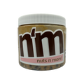 A clear jar of nut butter labeled "n'm" with a brown logo and pink accents, showcasing the product name "nuts n more!" against a black background.
