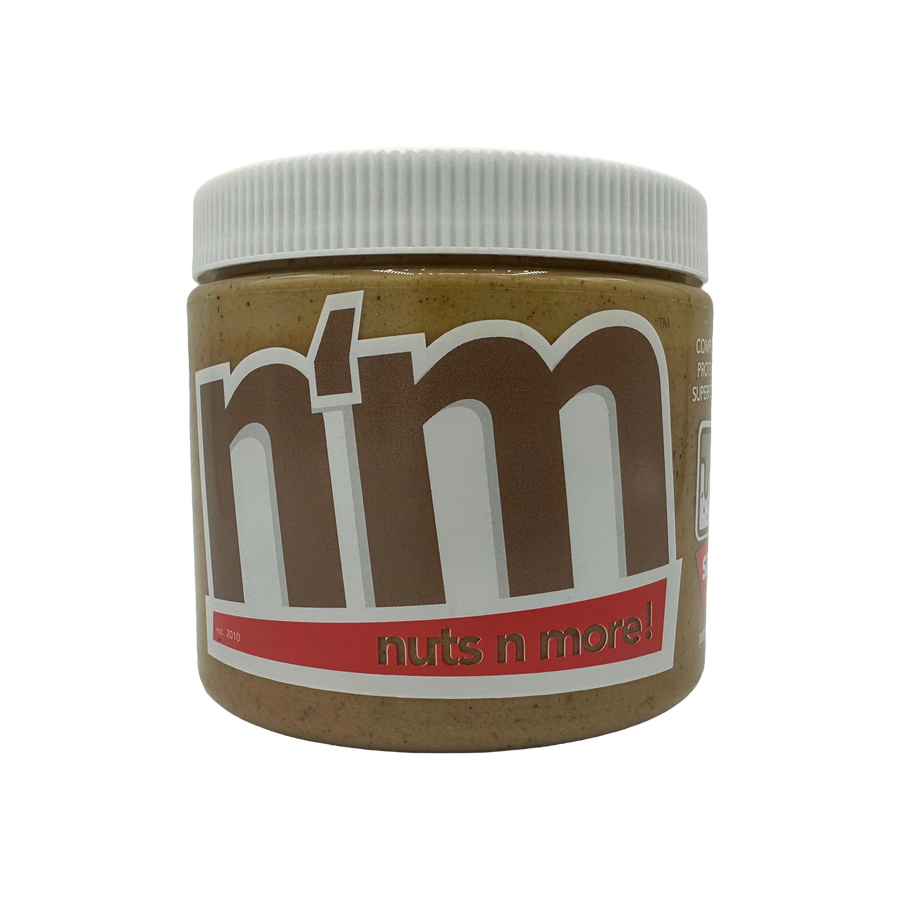 A close-up of a jar of "Nuts n More" nut butter, featuring a white lid and a label with bold brown and red text, set against a black background.