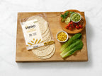 Hero flour tortillas with guacamole, tomatoes, corn, and lettuce on a wooden board.