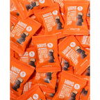 A pile of bright orange wrappers for WHIMS dark chocolate peanut butter cups, featuring a stacked image of the candy on the front, emphasizing its sweet and indulgent nature.