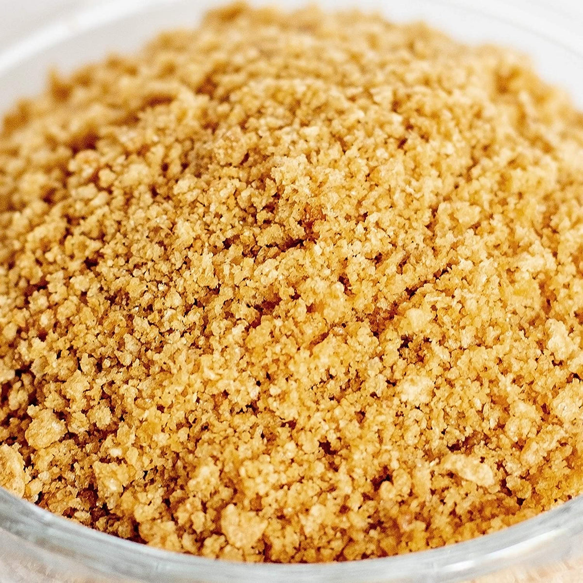 A close-up of finely ground brown sugar in a clear glass bowl, showcasing its granular texture and warm, golden-brown color.