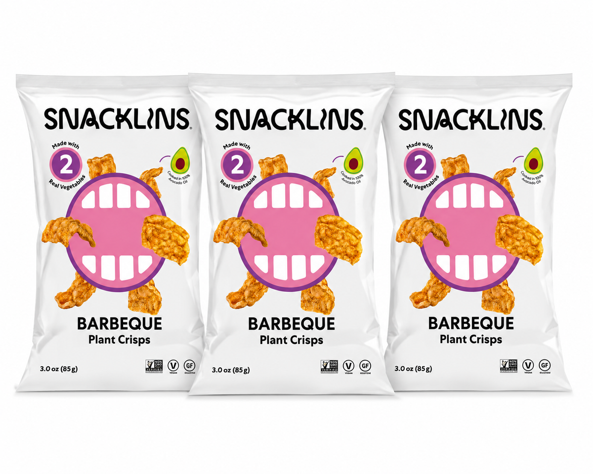 Three bags of Snacklins Barbeque Plant Crisps are displayed, featuring a playful design with a smiling mouth graphic and text highlighting that they are made with real vegetables and avocado oil.