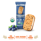 A pack of OLYRA Greek Yogurt Blueberry crème breakfast biscuits sits next to a biscuit filled with creamy yogurt and blueberries, highlighting its organic and nutritional benefits.