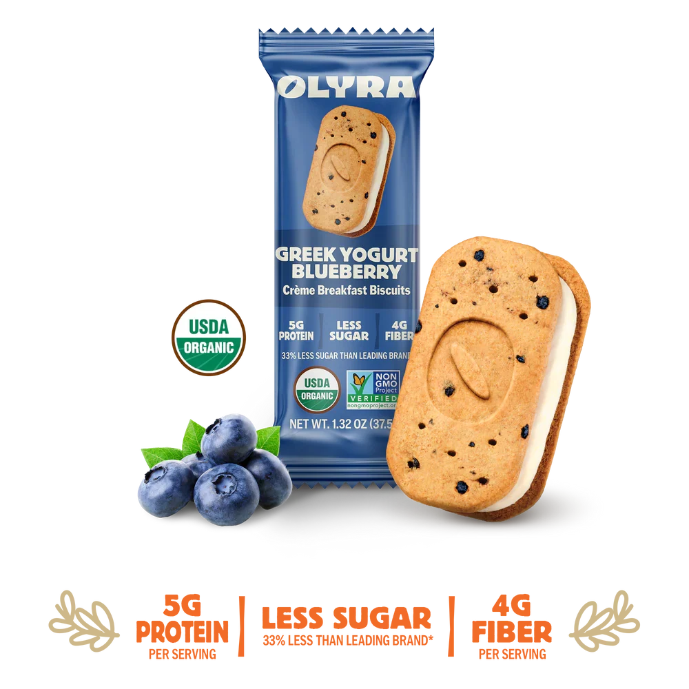A pack of OLYRA Greek Yogurt Blueberry crème breakfast biscuits sits next to a biscuit filled with creamy yogurt and blueberries, highlighting its organic and nutritional benefits.
