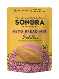 A yellow package of Sonora Keto Bread Mix features the product name prominently, with illustrations of bolillos and text highlighting low net carbs and preparation instructions.