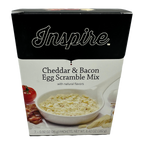 A box of Inspire Cheddar & Bacon Egg Scramble Mix features a bowl of the mix with a creamy texture, alongside a tomato and bacon, highlighting its natural flavors and serving suggestion.