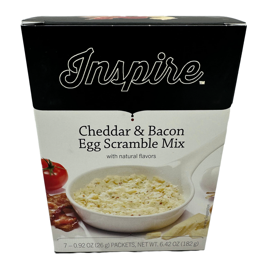 A box of Inspire Cheddar & Bacon Egg Scramble Mix features a bowl of the mix with a creamy texture, alongside a tomato and bacon, highlighting its natural flavors and serving suggestion.