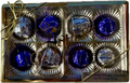 A gold box tied with a ribbon contains eight sugar-free cherry cordials, each wrapped in shiny blue foil, showcasing a premium chocolate gift suitable for special occasions.