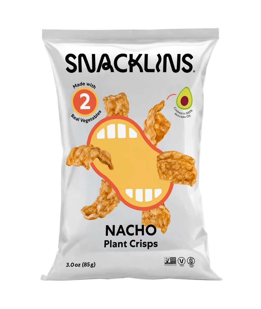 A bag of Snacklins Nacho Plant Crisps features a playful design with a cartoon mouth and crispy snacks, highlighting that it is made with two real vegetables and contains avocado oil.