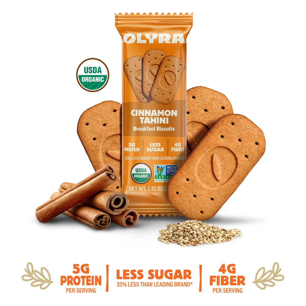 A package of Olyra Cinnamon Tahini Breakfast Biscuits is displayed with several biscuits, cinnamon sticks, and sesame seeds, highlighting 5g protein, less sugar, and 4g fiber on a black background.
