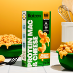A colorful box of Kaizen Protein Mac & Cheese sits next to a green bowl filled with cheesy pasta, against a bright orange background, highlighting its nutritional benefits and appealing presentation.