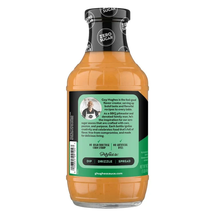 A clear bottle of Guy Hughes' zero sugar sauce features a vibrant orange color, with text highlighting its use for dipping, drizzling, or spreading, and a description of the brand's commitment to flavor and quality.