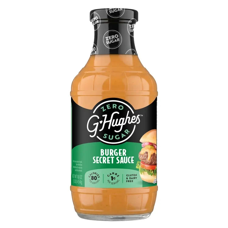 A clear bottle of G. Hughes Burger Secret Sauce, featuring a black label with green accents, displays nutritional information and a burger image, highlighting its zero sugar and gluten-free attributes.