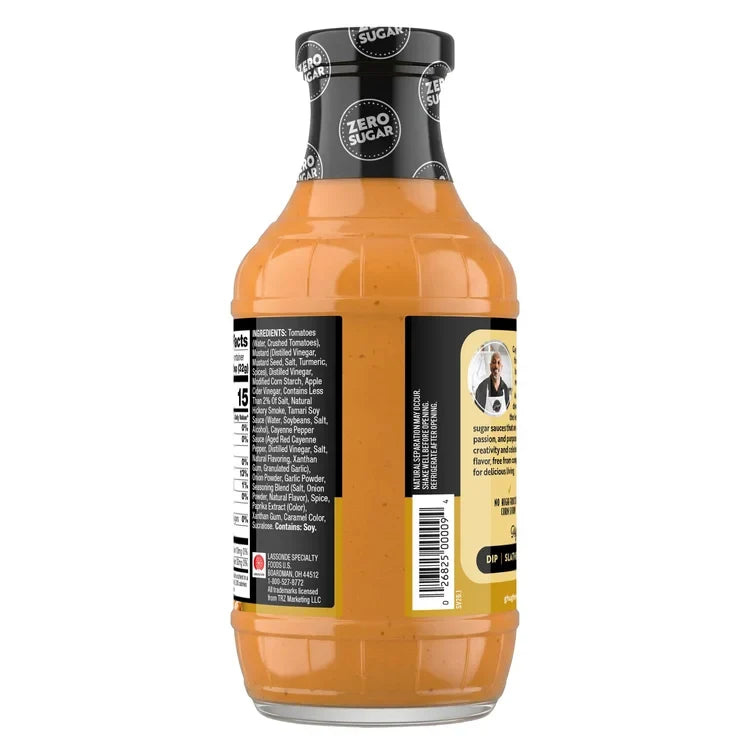 A clear glass bottle of zero sugar sauce with an orange hue, featuring a black label with ingredient information and a photo of a chef, placed on a white background.