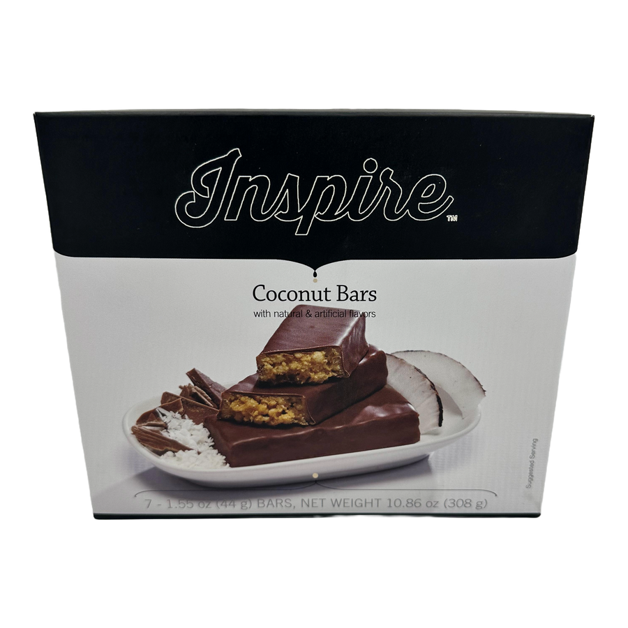 Inspire Coconut Bars, with natural and artificial flavors, packaged in a black box, featuring seven 1.55 oz bars, displayed on a plate with coconut flakes and pieces.