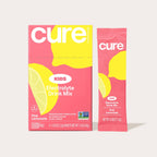 A pink and yellow box of Cure Kids Electrolyte Drink Mix, featuring a lemon graphic, displays six packets labeled "Pink Lemonade," emphasizing it's pediatrician formulated and plant-based.