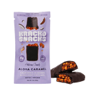 A purple package of Krack'd Snacks Aloha Caramel artisan candy, featuring a chocolate-covered bar with visible almonds and coconut caramel, sits next to a broken piece revealing its interior.