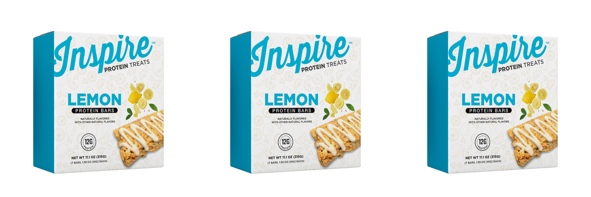 Three boxes of Inspire Lemon Protein Bars are displayed, each featuring a light blue design, the word "LEMON" prominently, and an image of a lemon-flavored protein bar drizzled with icing.