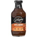 A clear bottle of G. Hughes Maple Brown flavored BBQ sauce, labeled as zero sugar, featuring a black and orange design with nutritional information, sits against a plain background.