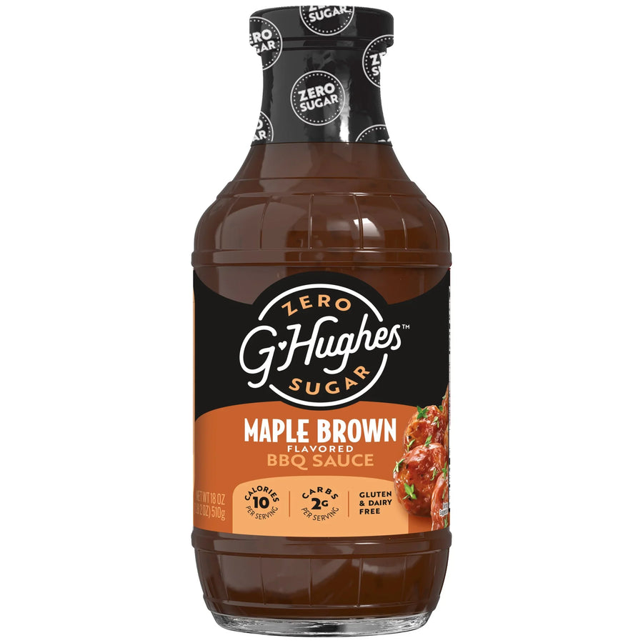 A clear bottle of G. Hughes Maple Brown flavored BBQ sauce, labeled as zero sugar, featuring a black and orange design with nutritional information, sits against a plain background.