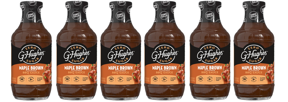 Five bottles of G. Hughes Maple Brown flavored BBQ sauce are lined up, each featuring a black cap and label highlighting "Zero Sugar," with details about calories and dietary information prominently displayed.