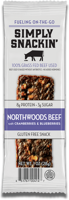 A packaged snack bar labeled "Simply Snackin' Northwoods Beef with Cranberries & Blueberries," highlighting its 100% grass-fed beef, gluten-free status, and nutritional information.