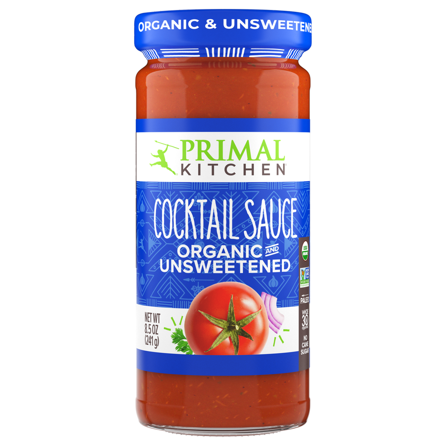 A clear glass jar of Primal Kitchen organic and unsweetened cocktail sauce features a vibrant red sauce with a tomato graphic, labeled prominently in blue and green.
