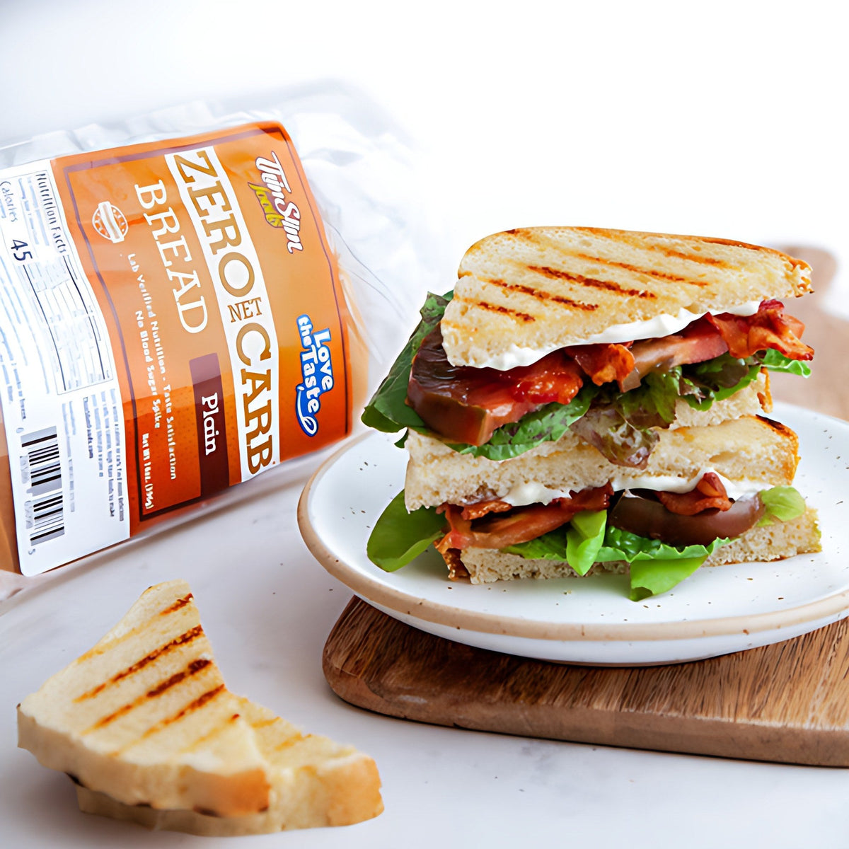 A grilled sandwich with lettuce and tomato beside a package of ThinSlim Foods Zero Net Carb Plain Bread.