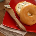 A sliced bagel with herb cream cheese on a red plate.