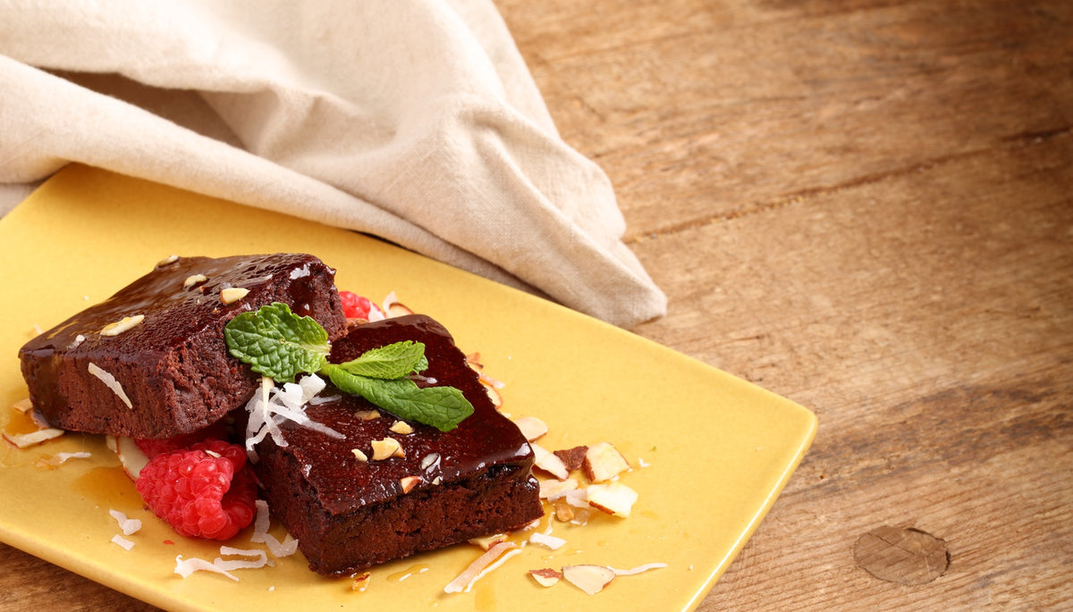 Two chocolate brownies served with raspberries, mint and shredded coconut on a yellow plate.